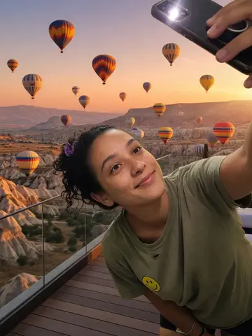 Exempel på Ballongsoluppgång: Personen står på en takterrass i soluppgången med dussintals färgglada luftballonger som svävar över klippiga dalar bakom sig.