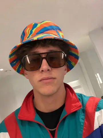 Exempel på Buckethatt-fit: Personen bär en färgglad buckethatt, stora tonade solglasögon och en vintage-vindjacka.