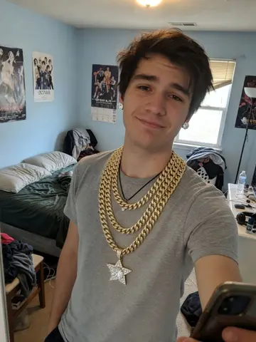 Exempel på Iced out: Personen bär flera tjocka guldkedjor i lager runt halsen, med ett stort diamanthänge och diamantörhängen.