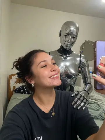Exempel på Robotpojkvän: Personen står bredvid en lång, människoliknande robot i krom som har armen om personens axlar som en pojkvän.