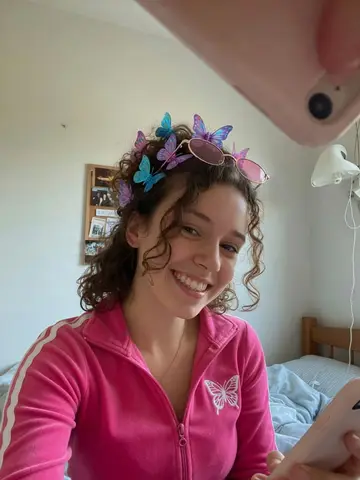 Exempel på Y2K-fit: Personen bär en Y2K-outfit med rosa velourjacka, små tonade solglasögon uppe på huvudet och fjärilsspännen i håret.